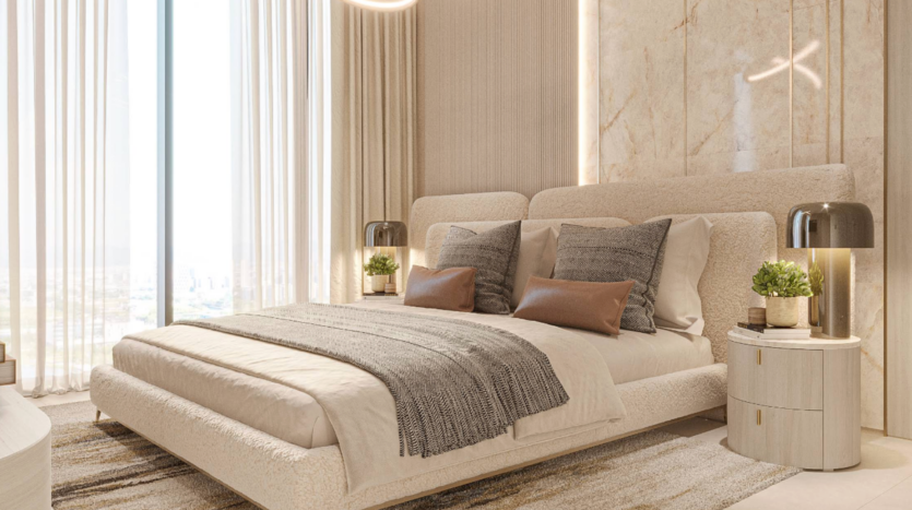 Luxurious room under a sunny sky with a king-size bed and beige and gray pillows. A marble wall adorns the back of the bed, round bedside tables with lamps and potted plants. Large windows with sheer curtains let in natural light.