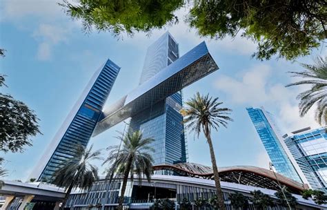 Die One Za'abeel Towers, ein architektonisches Meisterwerk in Dubai, erheben sich stolz mit einer einzigartigen horizontalen Luftbrücke, die die beiden Bauwerke miteinander verbindet, umgeben von Palmen und einem geschwungenen Glasgebäude unter vereinzelten Wolken.
