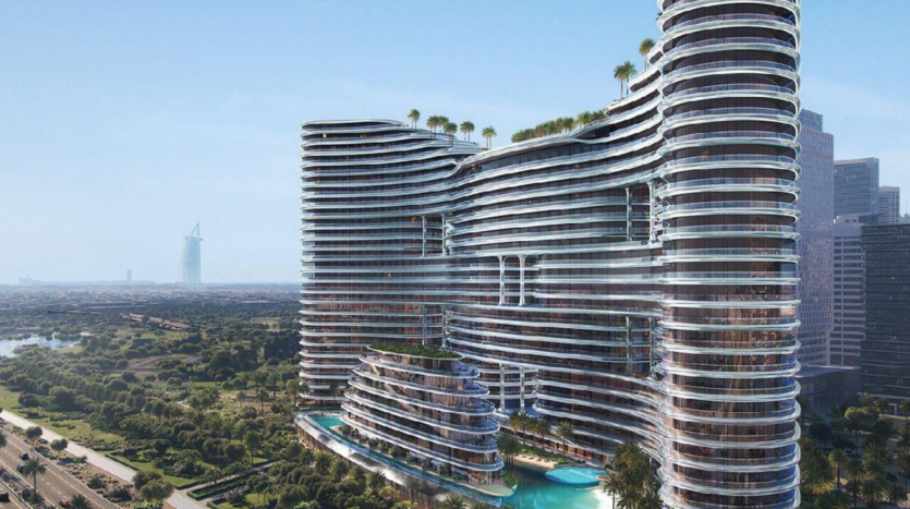 Binghatti Aquarise, un moderno rascacielos curvo con fachadas de cristal y tejados verdes, se alza junto a una piscina, rodeado de un paisaje exuberante, con una lejana torre emblemática visible contra el cielo azul.