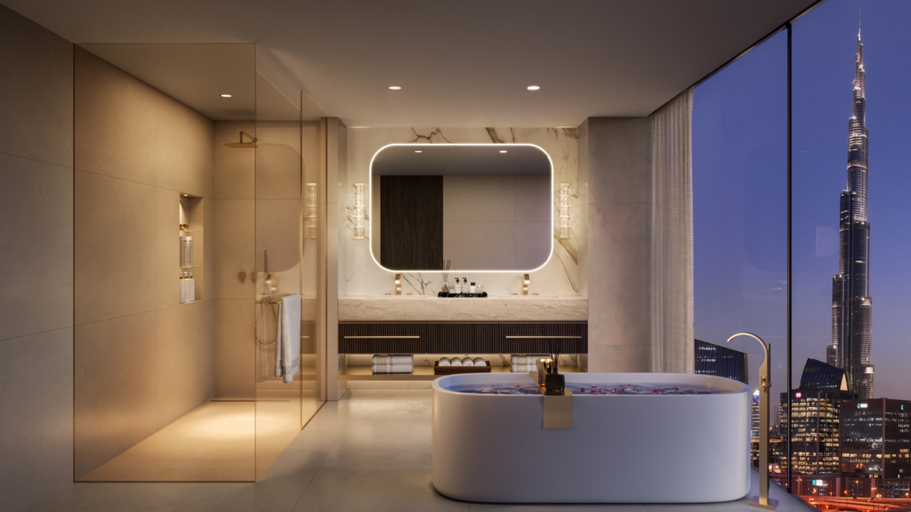 Lujoso cuarto de baño con una bañera independiente llena de pétalos de rosa, un gran espejo retroiluminado, una espaciosa ducha y ventanales que ofrecen vistas nocturnas de los tejados de la ciudad hasta el Burj Khalifa.