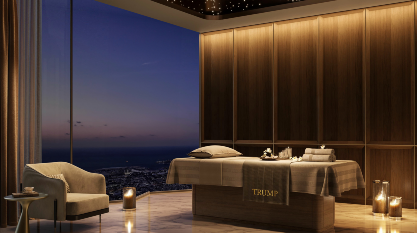Un lujoso spa con camilla de masajes, toallas, velas y mullidos sillones. Grandes ventanales ofrecen vistas de la ciudad y el océano al atardecer, y el techo está adornado con luces estrelladas.