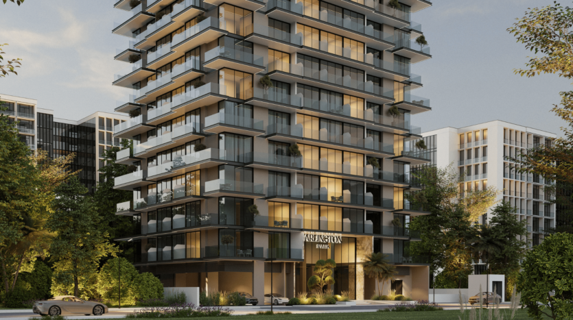 Immeuble résidentiel moderne de plusieurs étages avec de larges balcons vitrés, entouré d'arbres et de verdure, situé dans le parc Arlington de Dubaï. L'intérieur est baigné de lumière chaleureuse, quelques voitures sont garées devant et les bâtiments adjacents sont visibles en arrière-plan.