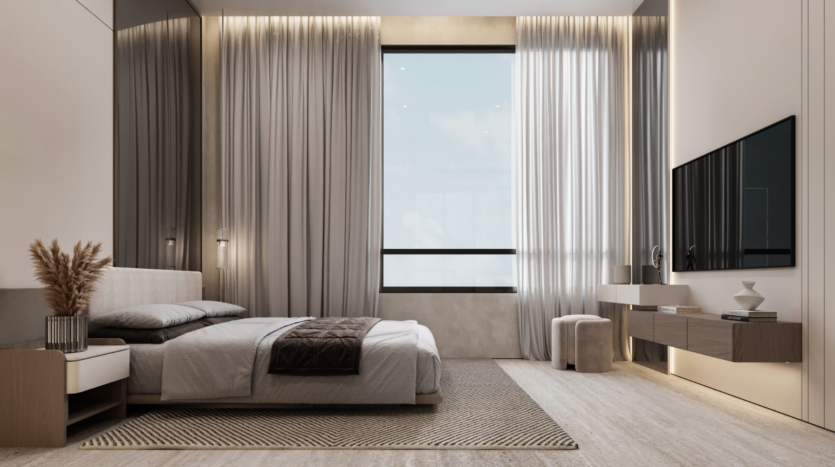 A modern, minimalist room in neutral tones, with a king-size bed, a bay window adorned with curtains, a wall-mounted TV, a hanging desk and subdued lighting. Decoration includes a vase filled with dried pampas grass and a textured rug.