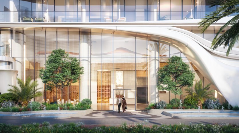 A person stands at the entrance to a modern, upscale building with tall glass windows, lush landscaping, trees and curved architectural elements, reflecting a luxurious, welcoming atmosphere.