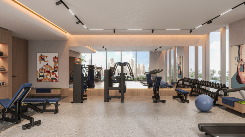 Modern gym with a variety of equipment, including benches, weight machines, dumbbells and a yoga ball. Large picture windows offer a view of the city, and workout posters decorate this bright, spacious room.