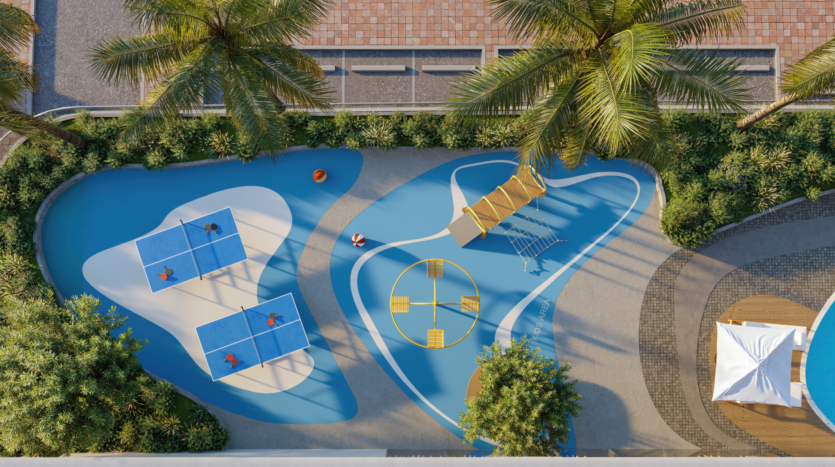 Aerial view of a colorful outdoor play area with two blue ping-pong tables, a yellow play structure, a four-seat merry-go-round and palm trees all around. Paths and greenery line the space.