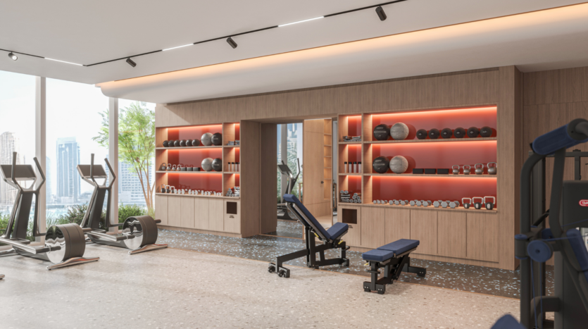 Modern gym with large windows, weight racks, medicine balls and benches. View of the city from outside. Warm lighting and well-organized fitness equipment create a clean, welcoming workout space.