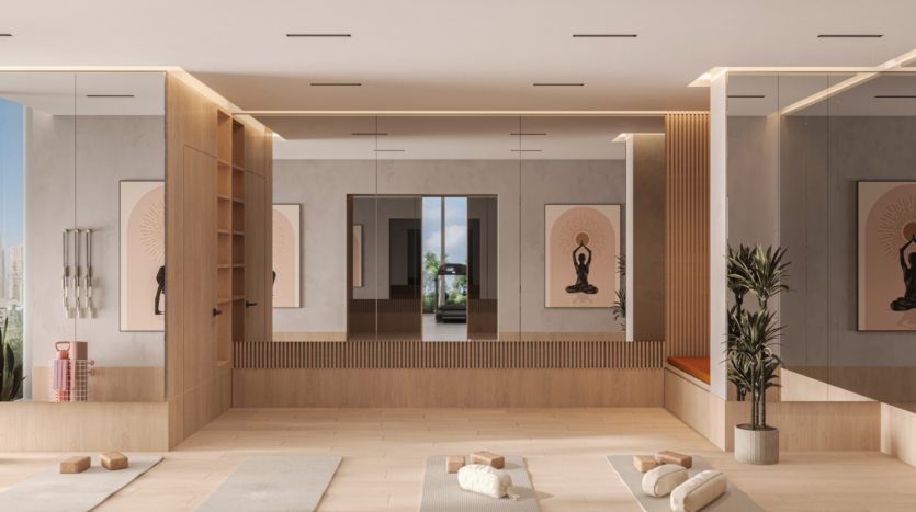 A modern yoga studio with parquet flooring, large mirrors, carefully rolled mats, meditation cushions, potted plants and wall decorations depicting a meditating figure. Natural light streams in through large windows.