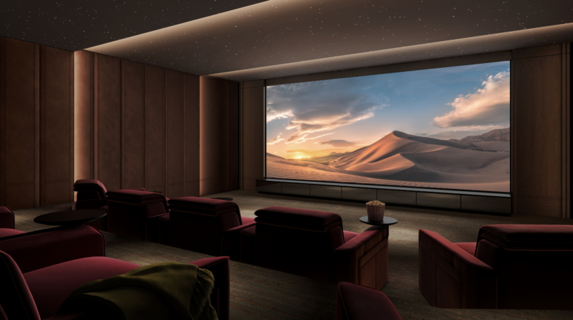 Un moderno cine en casa con asientos rojos reclinables frente a una gran pantalla que muestra un pintoresco paisaje desértico al atardecer. El techo está iluminado como si fueran estrellas, y en una mesa auxiliar hay un cubo de palomitas.