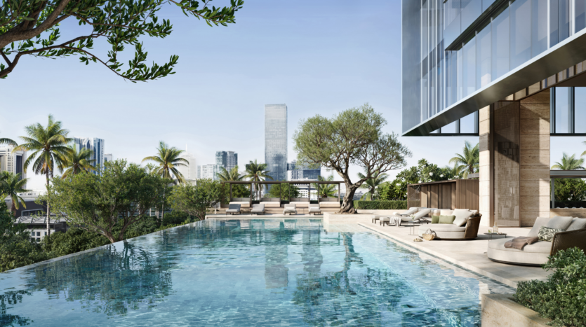Moderna piscina infinita en la azotea rodeada de tumbonas, vegetación y palmeras, con un edificio de cristal y el perfil de la ciudad al fondo.