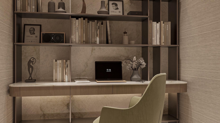 A modern home office at Provenza Residences Dubai includes a marble desk, green upholstered chair, laptop, books, decorative vases, framed photos and sculptures neatly arranged on shelves against a stone-textured wall.