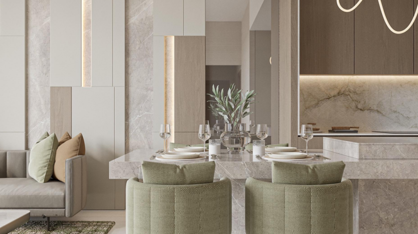 The modern dining room at Provenza Residences Dubai features a marble table for four, upholstered green chairs, a gray sofa with beige cushions and neutral-toned walls. A central plant and subdued lighting create a warm, elegant atmosphere.