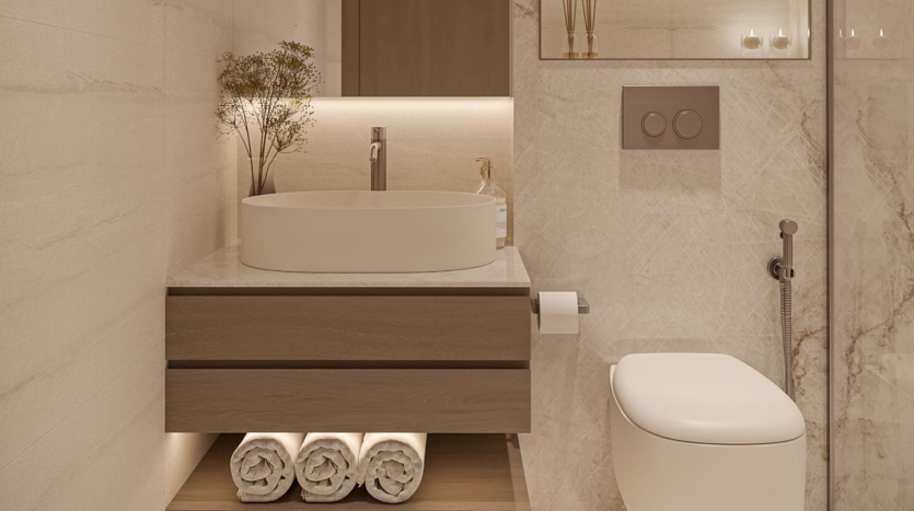 Modern bathroom at Provenza Residences Dubai featuring a round white sink on a wooden vanity, rolled towels underneath, wall-mounted toilet, neutral marble walls and subtle recessed lighting for a warm atmosphere.