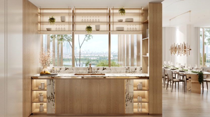 Cucina moderna con armadietti in legno chiaro, piani di lavoro in marmo, scaffali aperti con piante e stoviglie, un'ampia finestra con vista sull'isola di Wynwood Dubai e una sala da pranzo adiacente con un tavolo elegante e un lampadario.