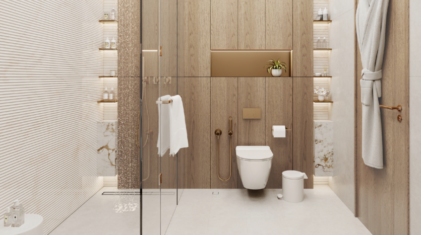Bagno moderno con accenti in legno chiaro e marmo, wc galleggiante, cabina doccia in vetro, portasciugamani, mensole con articoli da toilette, cestino bianco e accappatoio grigio appeso alla porta in legno.