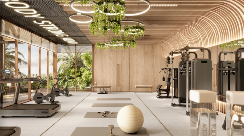 Palestra moderna con pareti e soffitto in legno chiaro, ampie finestre che lasciano intravedere il verde, attrezzi per gli esercizi, tappetino per lo yoga, palla di stabilità, piante da interno e apparecchi di illuminazione circolari che creano un'atmosfera accogliente, leggera e ariosa.
