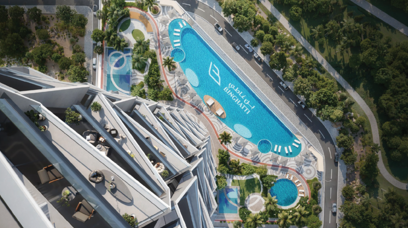 Aerial view of a modern rooftop pool with sun loungers, shaded areas and greenery, surrounded by a uniquely designed building and adjacent to a tree-lined road.