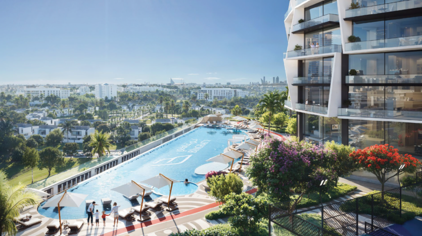 A large, modern outdoor pool with sun loungers and parasols, located next to the luxurious Binghatti Circle JVC apartment building, overlooks a cityscape with greenery and distant skyscrapers under a clear blue sky.