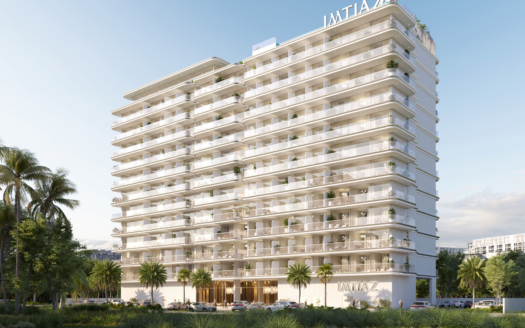 Ein modernes, weißes, mehrstöckiges Apartmenthaus - Cove Edition 6 von Imtiaz - mit großen Balkonen und Palmen an der Vorderseite erhebt sich unter einem klaren blauen Himmel. Das Schild "IMTIAZ" krönt die Spitze und erscheint über dem Haupteingang.