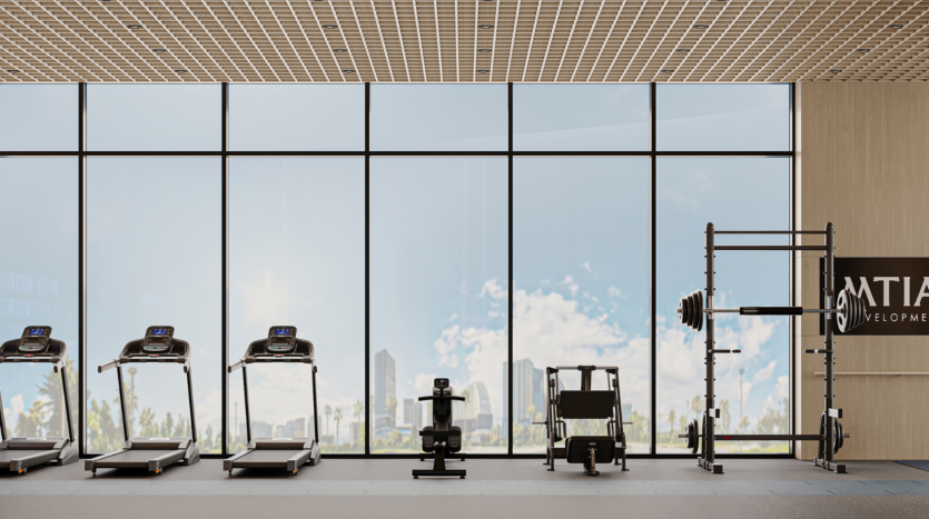 Salle de sport moderne avec de grandes fenêtres allant du sol au plafond, quatre tapis de course, un rameur, des appareils de musculation pour les jambes et un rack de squat avec des poids. La ligne d'horizon de la ville et le ciel bleu sont visibles à l'extérieur.