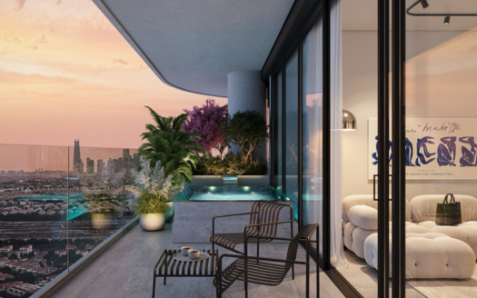 A modern balcony with glass balustrades, potted plants and a small pool overlooks the city at sunset. Two black chairs and a table are next to a comfortable indoor lounge with plush seating and contemporary artwork.