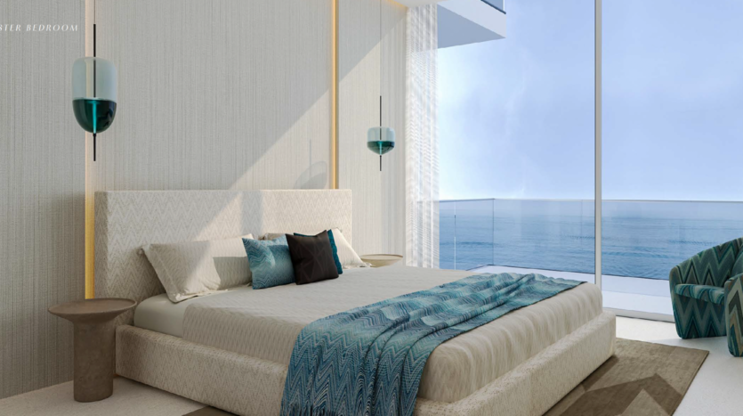 Modern room with king-size bed, blue and white bedding and decorative pillows. Large picture windows offer breathtaking ocean views from Dubai's Octa Isle, while natural light bathes the room. A small side table and chair complete the space.