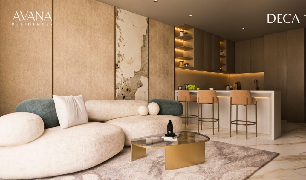 The modern living room at avana residences by Deca Properties in Dubai features a curved cream sofa, decorative cushions, a round glass coffee table and an open kitchen with high chairs. Neutral tones and marble accents create a luxurious atmosphere.
