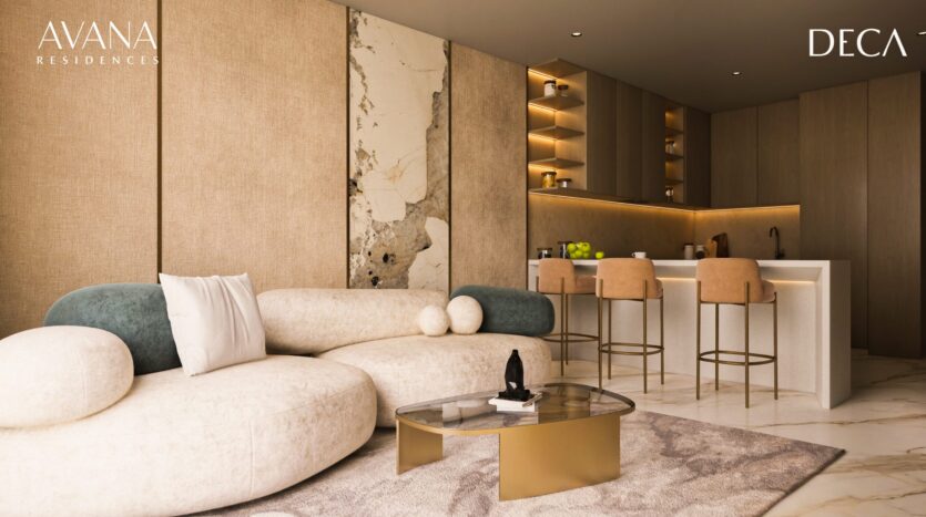 The modern living room at avana residences by Deca Properties in Dubai features a curved cream sofa, decorative cushions, a round glass coffee table and an open kitchen with high chairs. Neutral tones and marble accents create a luxurious atmosphere.