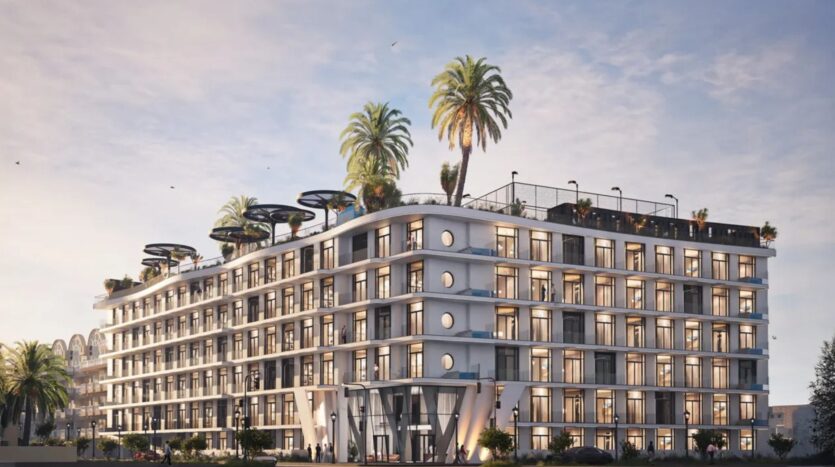 A modern multi-storey building with large windows and balconies, Avana Residences by Deca Properties in Dubai features rooftop palms, lush greenery and outdoor relaxation areas, all set against a backdrop of bright blue skies with a few clouds.