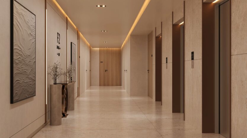 The modern, well-lit hallway of Ayaan Heights 1 by IGO features beige walls and floors, three elevator doors on the right, minimalist artwork and a decorative table with vases and branches on the left, with doors at the end.