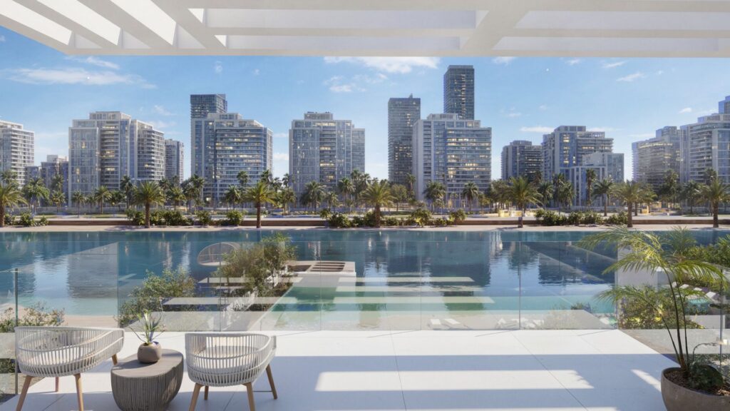 Enjoy the view from a modern balcony at Ayaan Heights 1 by IGO, with two chairs overlooking a clear blue waterway, swaying palms, and a skyline of tall modern buildings under a bright blue sky.