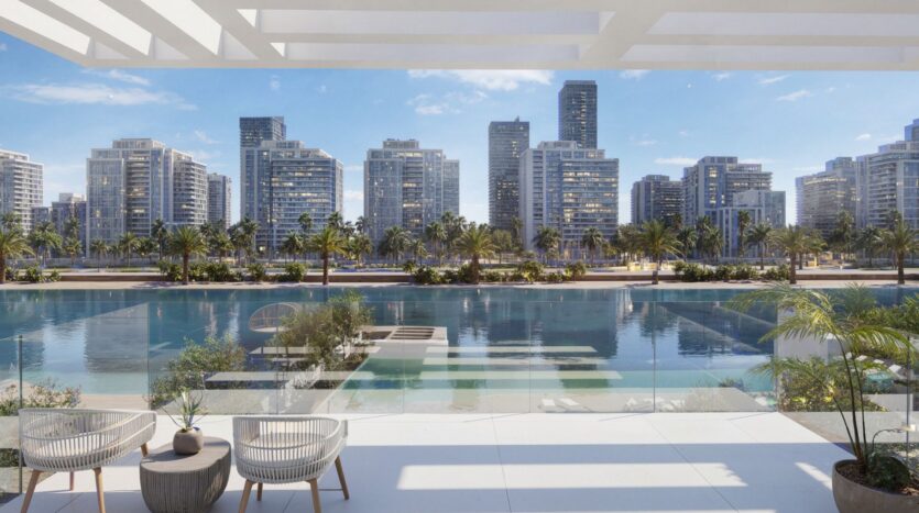 Enjoy the view from a modern balcony at Ayaan Heights 1 by IGO, with two chairs overlooking a clear blue waterway, swaying palms, and a skyline of tall modern buildings under a bright blue sky.