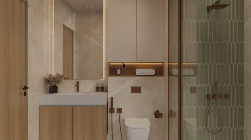 The modern bathroom in Ayaan Heights 1 by IGO features beige marble walls, a wooden vanity with sink, wall-mounted toilet, shelves with towels and decorative items, and a glass-enclosed shower with vertical tiles and bronze fittings.