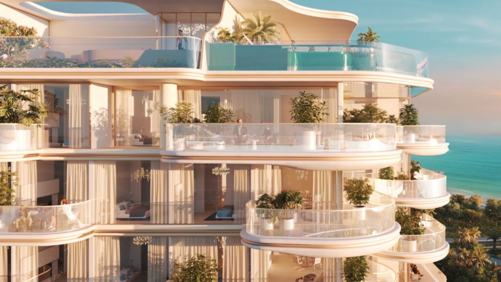 Beach Walk Grand 2, immeuble d'appartements de luxe moderne en bord de mer, dispose de grands balcons en verre, d'une végétation luxuriante, de fenêtres allant du sol au plafond et d'une piscine sur le toit avec vue sur l'océan au coucher du soleil.
