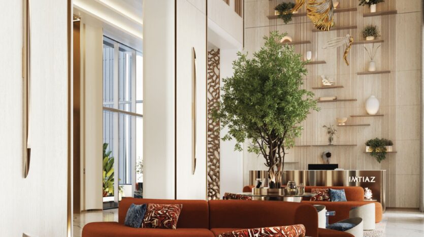 Un espace de vie moderne et haut de plafond à Beach Walk Grand comprend des canapés orange, des coussins à motifs, un grand arbre d'intérieur et des étagères décoratives avec des œuvres d'art et des plantes sur un mur crème. De grandes fenêtres inondent la pièce de lumière naturelle.
