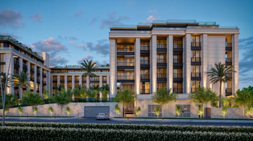 A modern multi-storey apartment building - Berkeley Square Prestige One - features large windows, balconies and lush vegetation with palm trees at the front. The well-lit facade glows at dusk when a car is parked on the street.