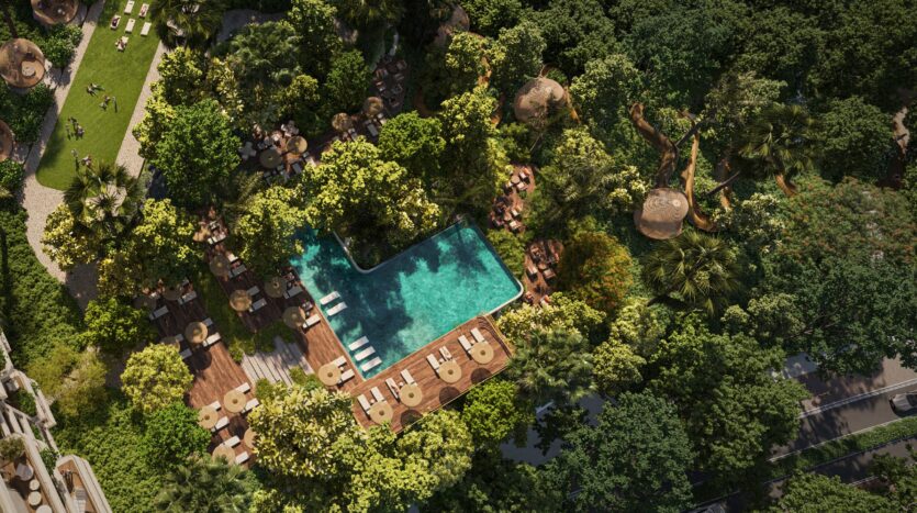 Vista aerea della piscina rettangolare di Talea by Beyond, circondata da alberi e da una vegetazione lussureggiante, con terrazze in legno, lettini e tavoli sparsi nel paesaggio, che creano un'atmosfera appartata e tropicale.