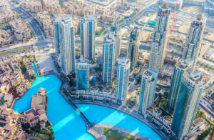 Dubai, Luftaufnahme von modernen Gebäuden, die einen großen türkisfarbenen künstlichen Pool umgeben, mit sichtbaren Straßen und Baustellen im Hintergrund, die die Auswirkungen der steigenden Mieten auf diese dynamische Stadtlandschaft verdeutlichen.