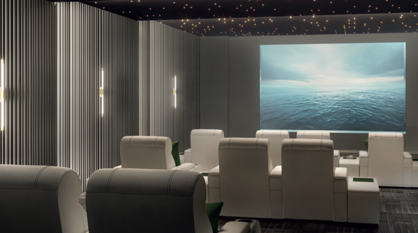 A modern home cinema room with white reclining armchairs facing a large screen displaying an ocean scene. The walls feature vertical light strips and the ceiling is decorated with small star-shaped lights.