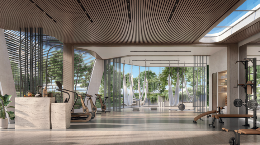 Modern gym with wood accents, large windows and abundant natural light. Equipment includes treadmills, stationary bikes, weights and aerial yoga hammocks. Trees and greenery are visible outside.