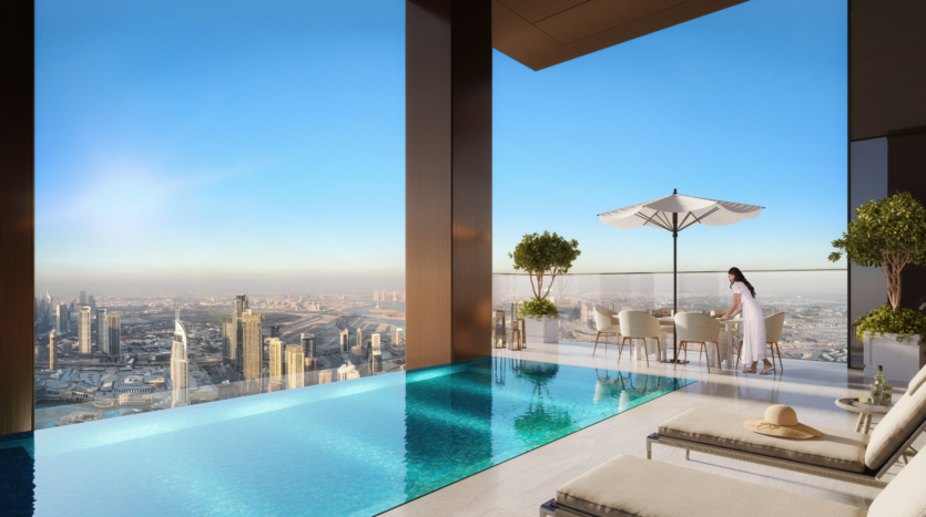 Una lussuosa piscina a sfioro sul tetto si affaccia sullo skyline di una città al sorgere del sole. Una donna è in piedi accanto a un tavolo sotto un ombrellone bianco, mentre due lettini sono posizionati accanto alla piscina. In lontananza si vedono alti edifici.