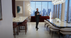 Ein Mann im Anzug steht in einem modernen, luxuriösen Apartment im Waldorf Astoria Dubai, mit Marmortheken, einem großen Esstisch und Fenstern, die vom Boden bis zur Decke reichen und auf eine atemberaubende Skyline blicken.