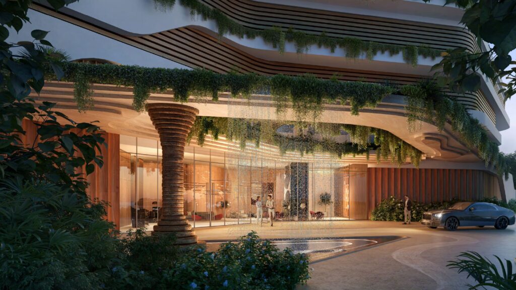 Un ingresso moderno con linee architettoniche curve, verde pensile, porte di vetro e una colonna decorativa accoglie i visitatori di Talea by beyond. Un'illuminazione calda e una piccola fontana circolare creano un'atmosfera accogliente con un'auto parcheggiata sul davanti.