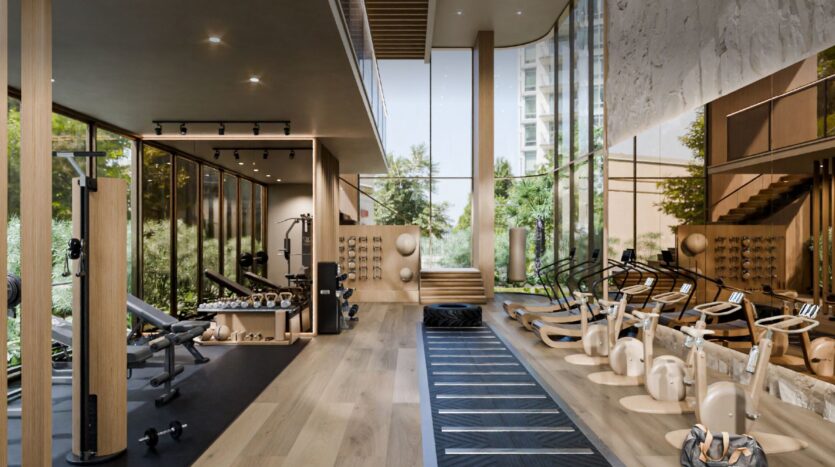 Moderna palestra del Talea by Beyond con grandi finestre, pavimenti in legno e luce naturale. Dispone di una varietà di attrezzature per l'esercizio fisico, tra cui pesi, macchine, vogatori e palle d'equilibrio. Il verde è visibile all'esterno.