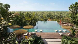 Una piscina a sfioro immersa nel verde a Talea by Beyond, con lettini di paglia e ombrelloni che si affacciano su una foresta. Le persone si rilassano a bordo piscina mentre il mare scintilla in lontananza sotto un cielo azzurro e limpido.
