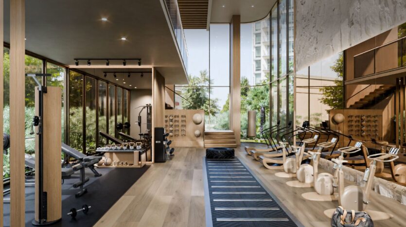 Moderna palestra a Talea by beyond con grandi finestre, pavimenti in legno e una serie di attrezzature per l'esercizio fisico. Lo spazio luminoso è pieno di luce naturale e offre una vista sul verde esterno.
