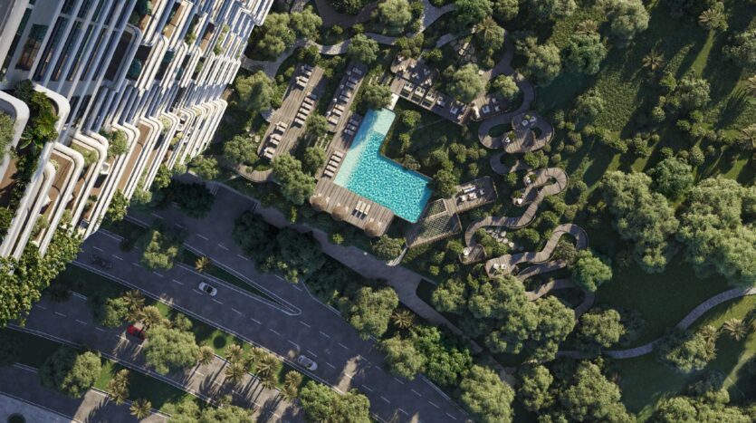 Vista aerea del moderno edificio Talea by Beyond accanto a una piscina sul tetto, circondata da lettini, passerelle e alberi verdi, con una strada e delle auto visibili nella parte inferiore dell'immagine.