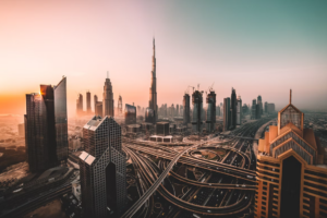 Stadtlandschaft von Dubai bei Sonnenuntergang, mit dem Burj Khalifa und modernen Wolkenkratzern. Komplexe Autobahnen und Straßen schlängeln sich durch die Stadt, mit warmem Licht auf der linken Seite und kühleren Tönen auf der rechten Seite.