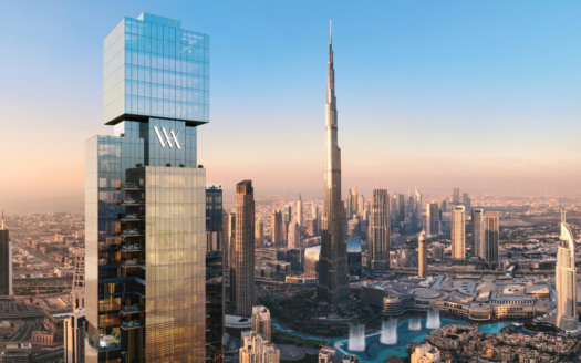 A large modern skyscraper bearing the "Waldorf Astoria" logo stands in the foreground, overlooking a cityscape composed of the Burj Khalifa and surrounding Dubai buildings, under a clear sky at sunset.