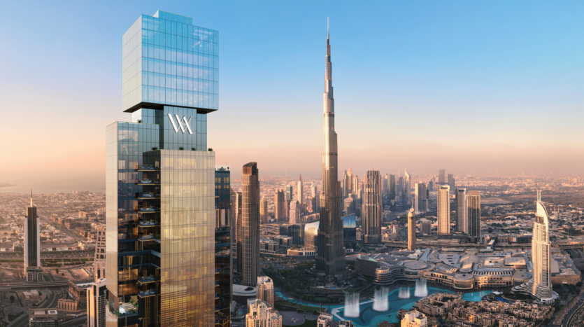 Un grande grattacielo moderno con il logo "Waldorf Astoria" si erge in primo piano e domina un paesaggio urbano composto dal Burj Khalifa e dagli edifici circostanti di Dubai, sotto un cielo limpido al tramonto.